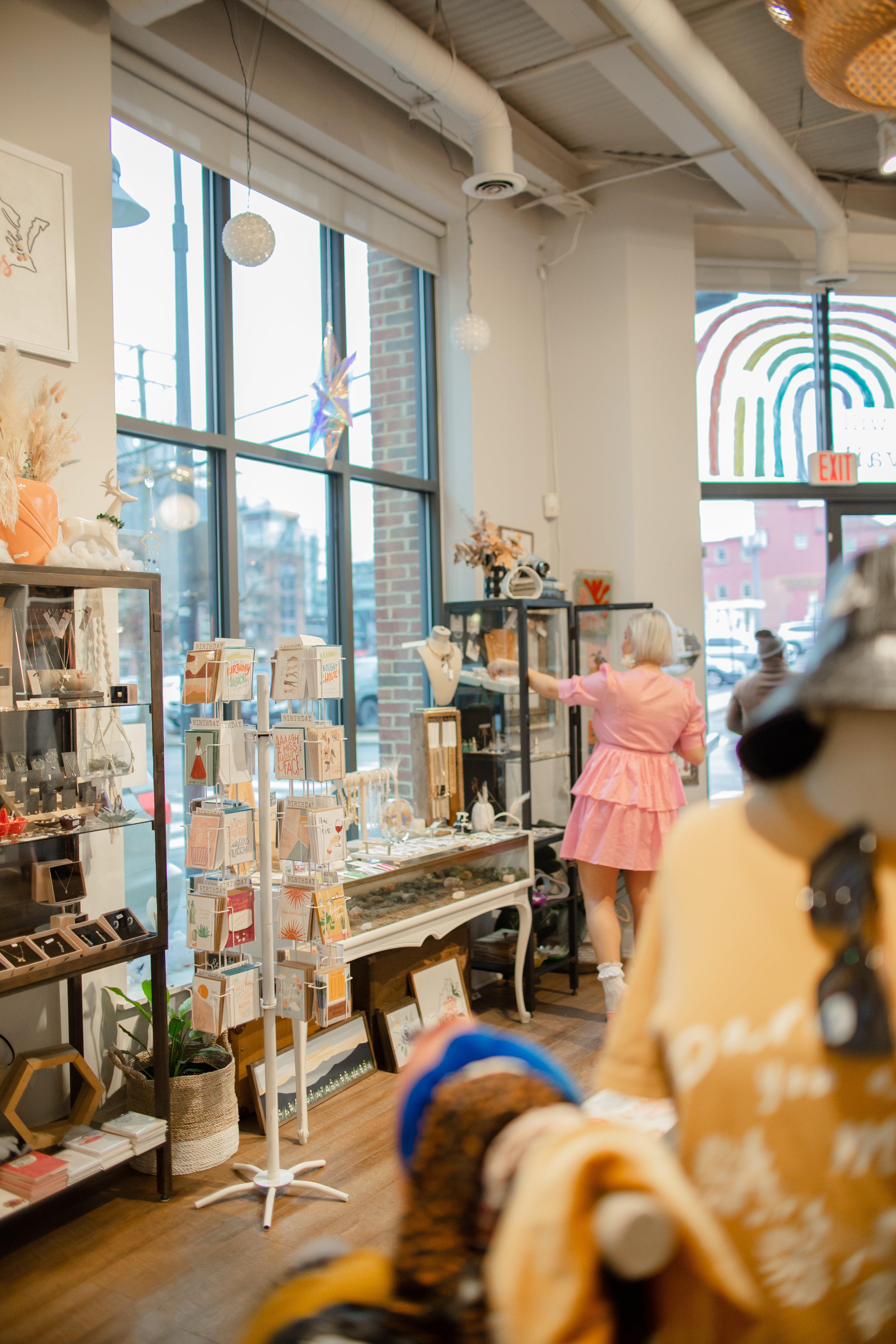 Linnea White, DarlingxDashing shop owner, in a pink dress organizing the accessory section of the shop