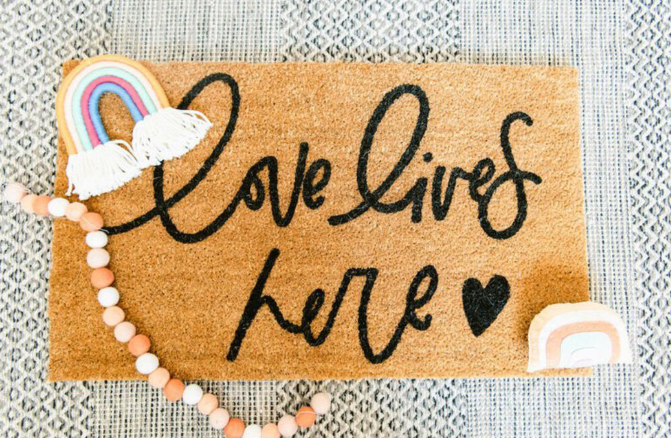 brown doormat that reads "love lives here" with a heart, made by pencraft + post