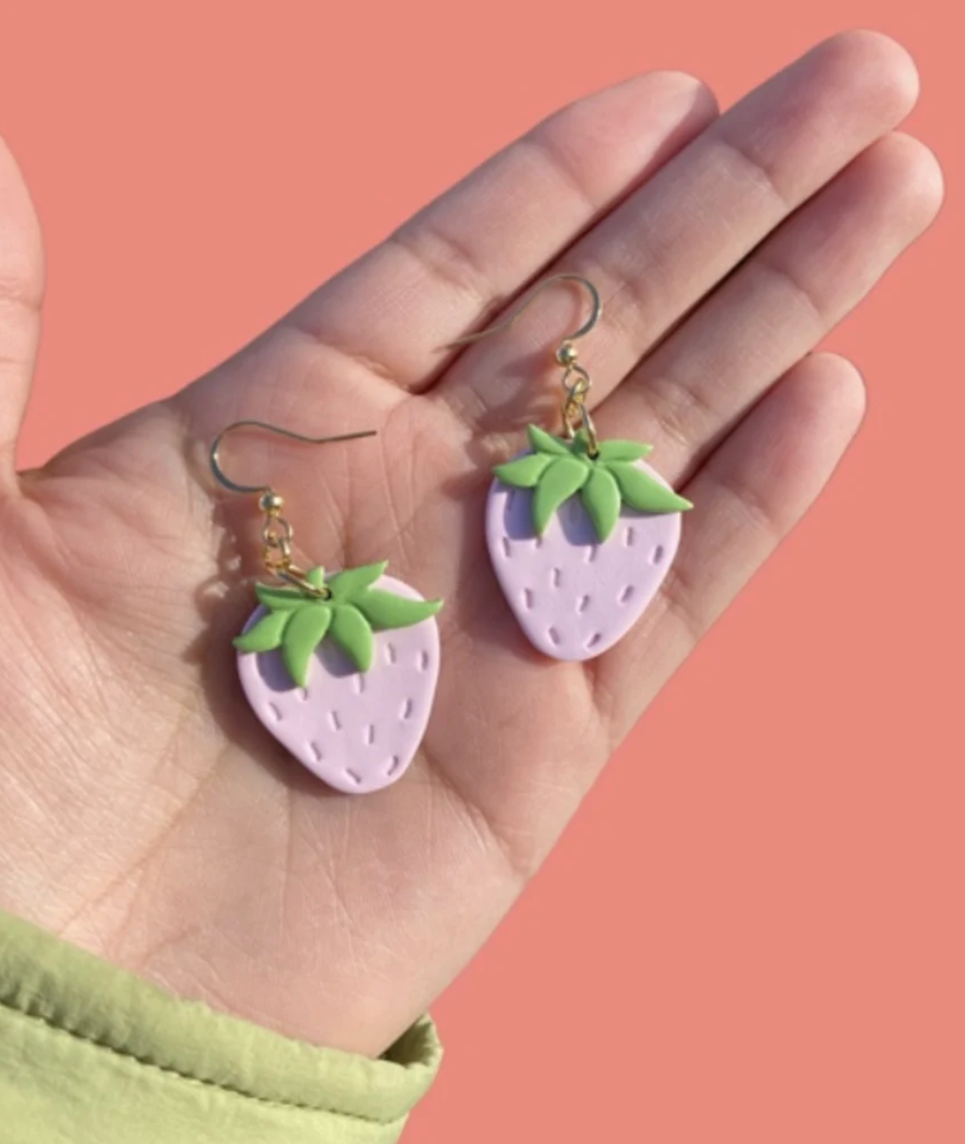 Person holding pink and green clay strawberry earrings, created by amoeba clay