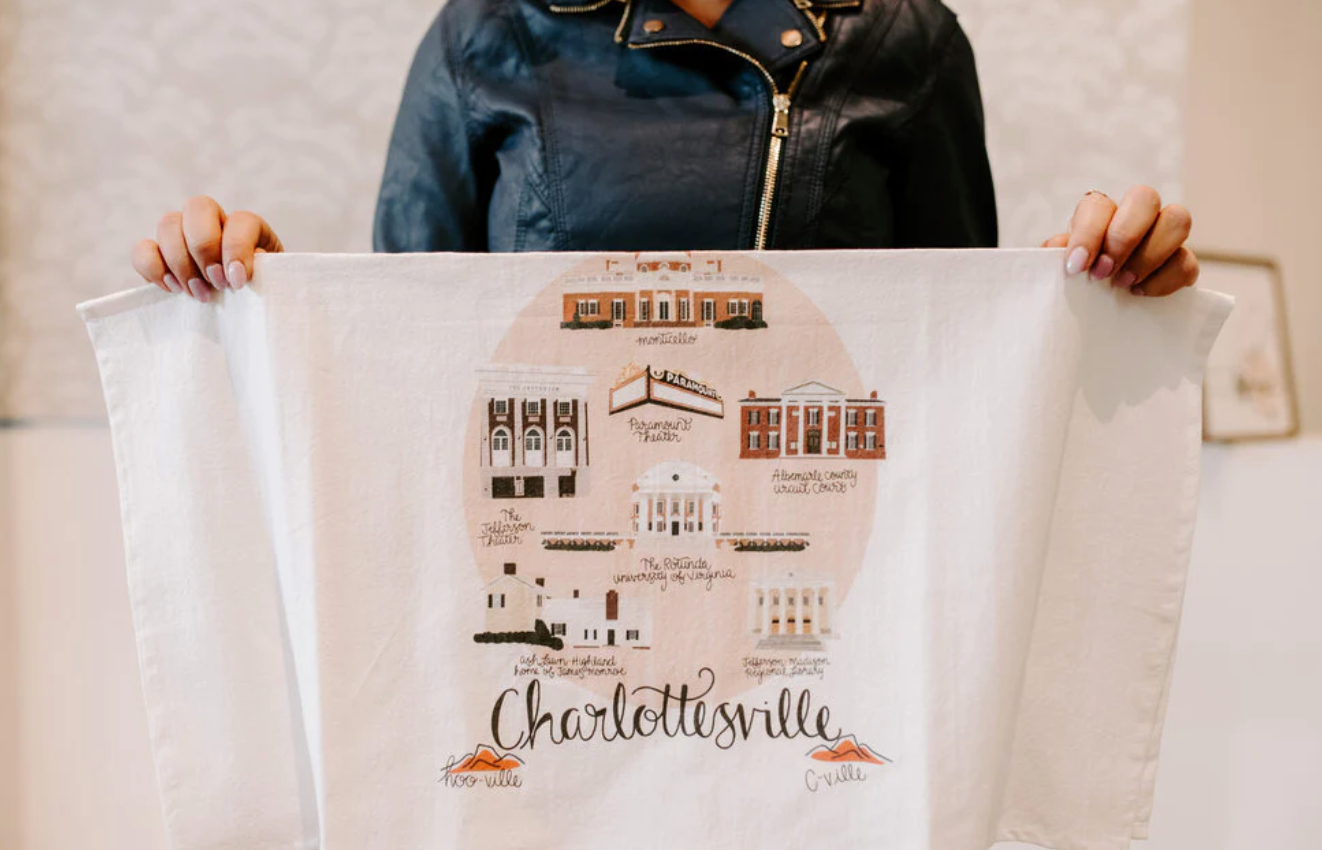 person holding up Charlottesville tea towel with illustrated landmarks, made by Lane Paper Works