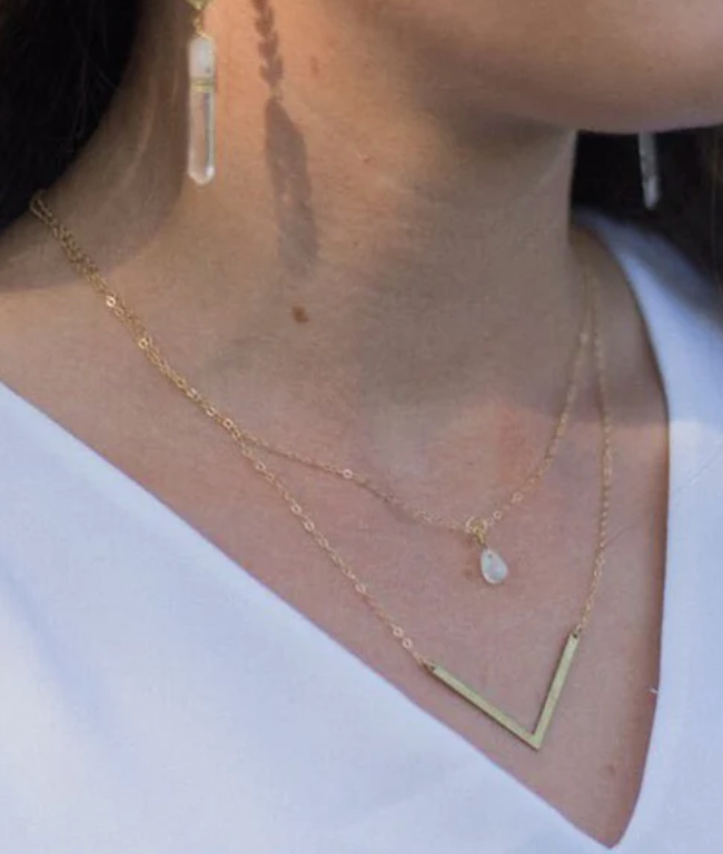 woman wearing dainty gold necklaces and earrings featuring crystals, made by sojourn well
